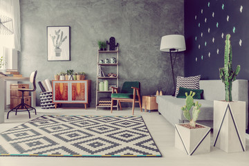 Real photo of living room interior with cactuses, grey sofa, big lamp, geometric carpet and texture wall