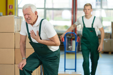 Senior warehouseman having a heart attack at work, young colleague running to help him