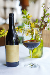 Bottle and glass of red wine on the table with spring decor. Restaurant table setting.