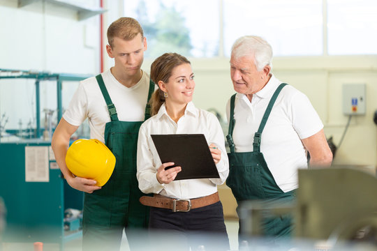 Two stock workers in dark green uniforms and office manager checking delivery