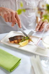 A man in a restaurant is eating grilled salmon. Close-up.