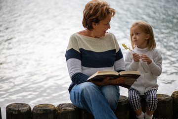 grandmother and granddaughter read a book and dream on the lake