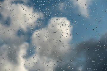 Raindrops on a window glass against the background of clouds. Weather forecast.