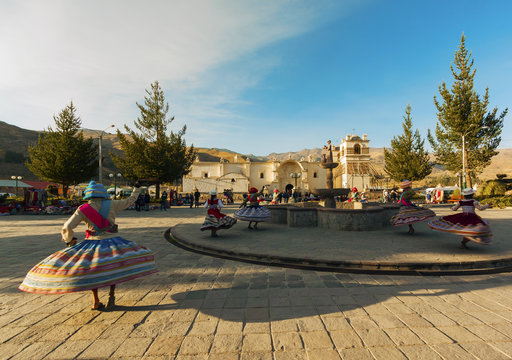 Peru, Chivay, joung girls dancing in traditional dresses around a fountain on the village square