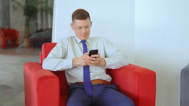 portrait caucasian business man sitting in a red chair scrolls news feed in social media