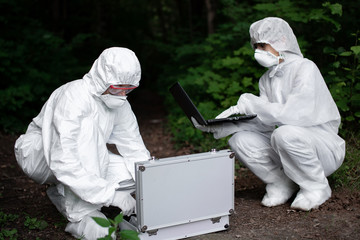Ecological problem. Pollution. Examine soil. Scientist working in forest in protective mask and suit taking water and soil samples. Chemist makes an analysis of the environment for radiation. 