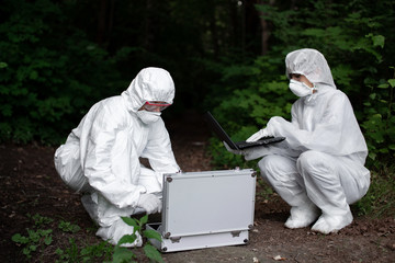 Ecological problem. Pollution. Examine soil. Scientist working in forest in protective mask and suit taking water and soil samples. Chemist makes an analysis of the environment for radiation. 