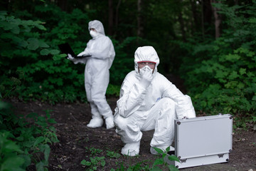 Ecological problem. Pollution. Examine soil. Scientist working in forest in protective mask and suit taking water and soil samples. Chemist makes an analysis of the environment for radiation. 