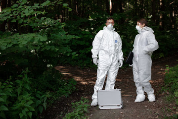 Fototapeta premium Ecological problem. Pollution. Examine soil. Scientist working in forest in protective mask and suit taking water and soil samples. Chemist makes an analysis of the environment for radiation. 