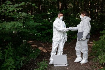 Fototapeta premium Ecological problem. Pollution. Examine soil. Scientist working in forest in protective mask and suit taking water and soil samples. Chemist makes an analysis of the environment for radiation. 