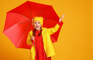 young happy emotional cheerful child girl laughing  with red umbrella   on colored yellow...