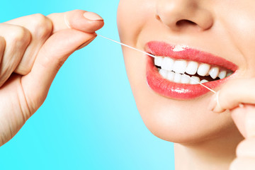 Young beautiful woman is engaged in cleaning teeth. Beautiful smile healthy white teeth. A girl holds a dental floss. The concept of oral hygiene.
