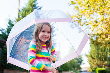 Kids in fall. Portrait of a cute little baby girl walking near the house with an umbrella in the rain on a warm autumn day. children have fun outdoor during bad weather in the rain