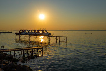 Balaton lake over sunset with pedal boats on a pier and sunbeam in Hungary