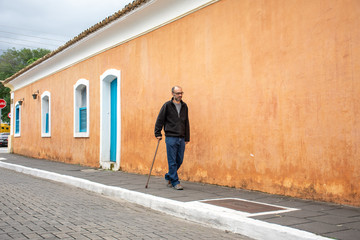 Fototapeta na wymiar Disabled man walks with walking stick and difficulty on the street
