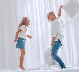 close up. mom and daughter have a pillow fight on the bed