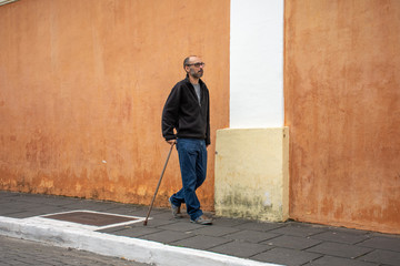 Disabled man walks with walking stick and difficulty on the street