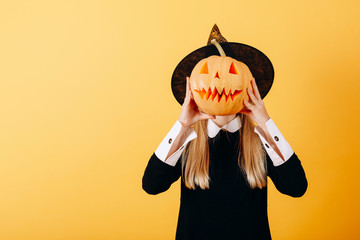 Woman standing against a yellow background  holding pumpkin and hiding her face
