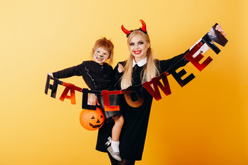 Devil woman standing against a yellow background with a little girl and holding a postcard Halloween