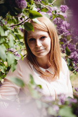 Fototapeta premium Beautiful young woman smiling with lilac flowers around in park