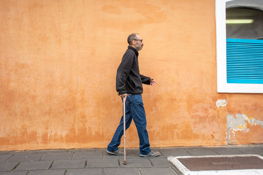 Disabled man walks with walking stick and difficulty on the street