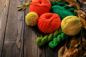 Composition with yarn balls and autumn leaves on wooden background