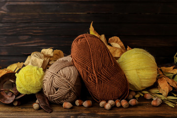 Composition with yarn balls and autumn leaves on wooden background