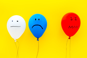 Negative emotions concept. Balloons with drawn faces on yellow background top view