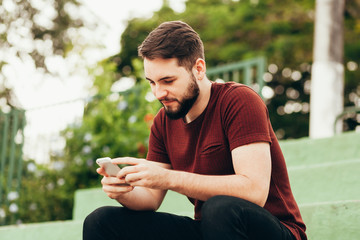 Attractive young smiling man using phone in a public park