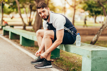 Young runner sitting in public park tying his shoelaces