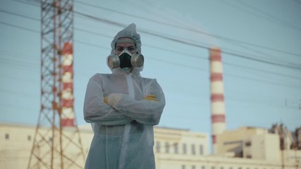 The scientist put on a respirator and a protective gown. Student girl showing thumbs up on the background of the plant. Atmospheric pollution. Coronavirus in a pandemic, COVID-19.
