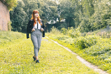 Cute young girl in a black leather jacket with curly red hair and a fringe walks relaxedly in a...