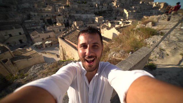 handsome tourist man travelling in south of italy, taking selfie photo in Matera, Basilicata, unesco site, capital of culture 2019. concept of travel in Italy. slow motion video