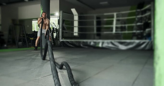 Fitness athlete uses battle ropes in training. Intense workout exercise. Slow motion