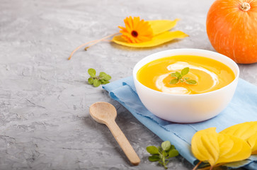 Traditional pumpkin cream soup with in white bowl on a gray concrete background with blue napkin. side view, selective focus.