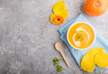 Traditional pumpkin cream soup with in white bowl on a gray concrete background with blue napkin. top view