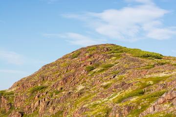 A gentle mountain on which grass and moss grow under a soft blue sky. Rock, dotted with winds and rains proudly rises.