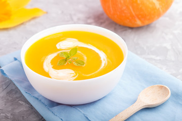 Traditional pumpkin cream soup with in white bowl on a gray concrete background with blue napkin. side view, selective focus.