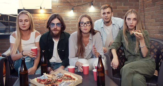 Group of friends enjoying pizza and watching sports game on television, making winner gesture, happiness