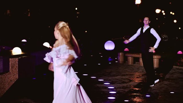 Cool beautiful girl and her partner dancing at night at the fountain. Very beautiful dance.