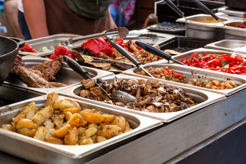 A counter with metal trays containing grilled food. Food and cooking equipment at a street food festival