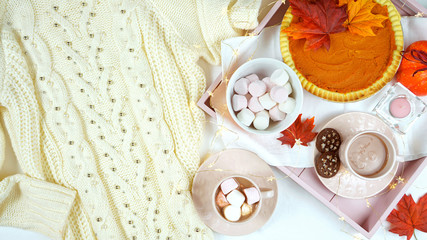 Cozy autumn Thanksgiving in bed flatlay overhead with cosy sweater, tray with pumpkin pie and hot chocolate and copy space.