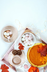 Cozy autumn Thanksgiving in bed flatlay overhead with tray of pumpkin pie and hot chocolate with marshmallows, vertical copy space.