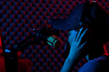 Young Adult sing a cover Song on Youtube. Woman connect social media with professional equipment such as e-sport gaming keyboard, mouse, monitor, speaker, camera, studio, dark red blue theme © Jade