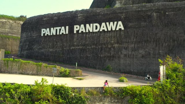 Active lifestyle travel woman sitting on the edge of a mountain cliff and posing. Pantai Pandawa Beach Bali. 4k. Aerial view.
