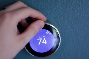 Male Hand changes temperature of smart home thermostat on blue wall in Fahrenheit  .