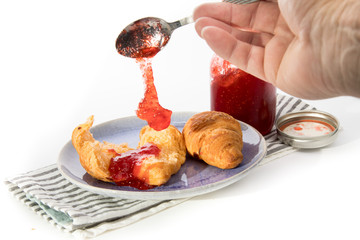 two cheese croissants on a plate with a jar of home made strawberry jam isolated on white
