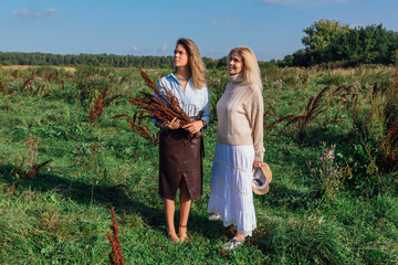 Portrait of two beautiful women in a field in late summer. Beautiful girls standing next to each other and holding bouquet made of dry brown plants.