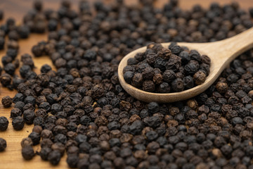 Dry heap black pepper isolated on wooden chopper board with wooden spoon
