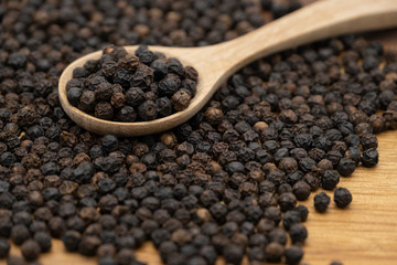 Dry heap black pepper isolated on wooden chopper board with wooden spoon